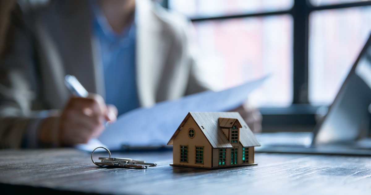 Symbolbild Kosten beim Hausverkauf: Modell eines Hauses steht auf Tisch mit Schlüssel
