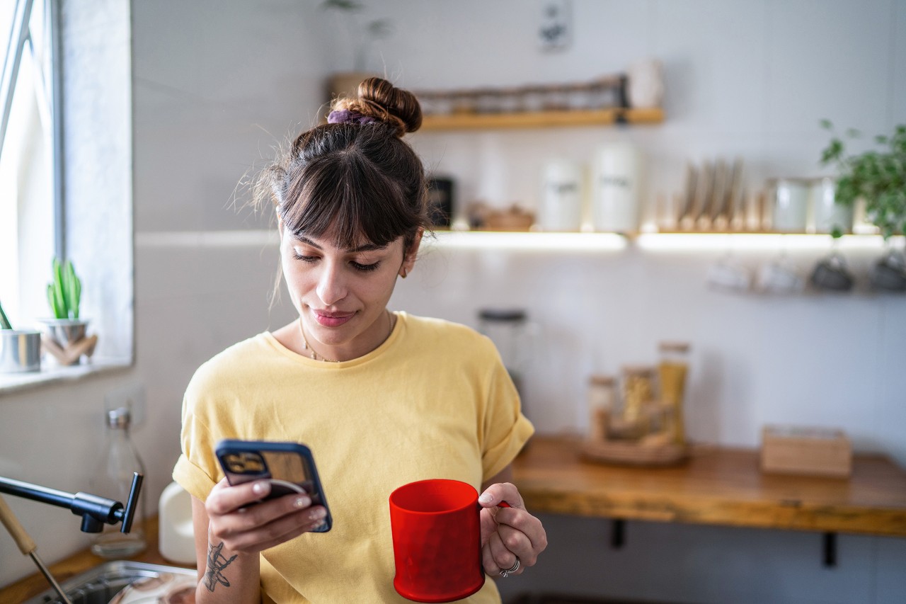 Donna in cucina con smartphone e tazza in mano