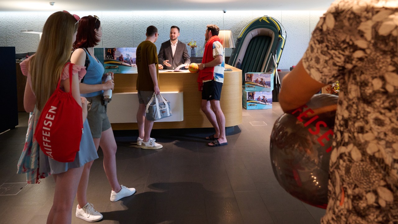 Schalterhalle in Thun mit Leuten vor dem Schalter. Sie holen ein Gummiboot ab, welches sie von der Bank geschenkt kriegen.